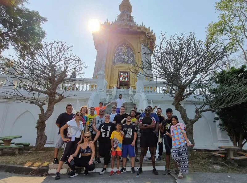 A diverse group of Kombat Group BJJ camp participants pose together in front of a beautiful temple in Pattaya, Thailand. The image captures the camaraderie and cultural exploration that complement the intense training sessions, showcasing the holistic experience provided by the BJJ training camp.