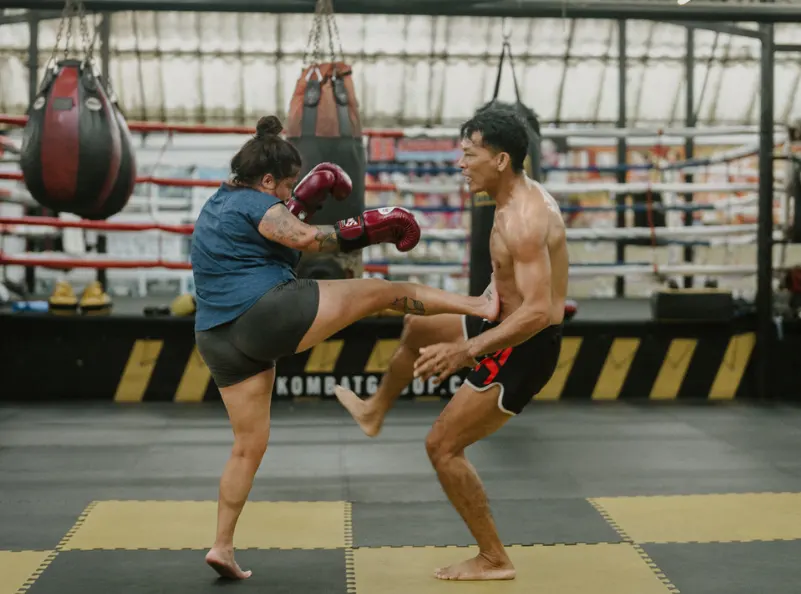 A female student delivers a strong front kick while training Muay Thai with her coach at Kombat Group, a top martial arts gym in Pattaya, Thailand.